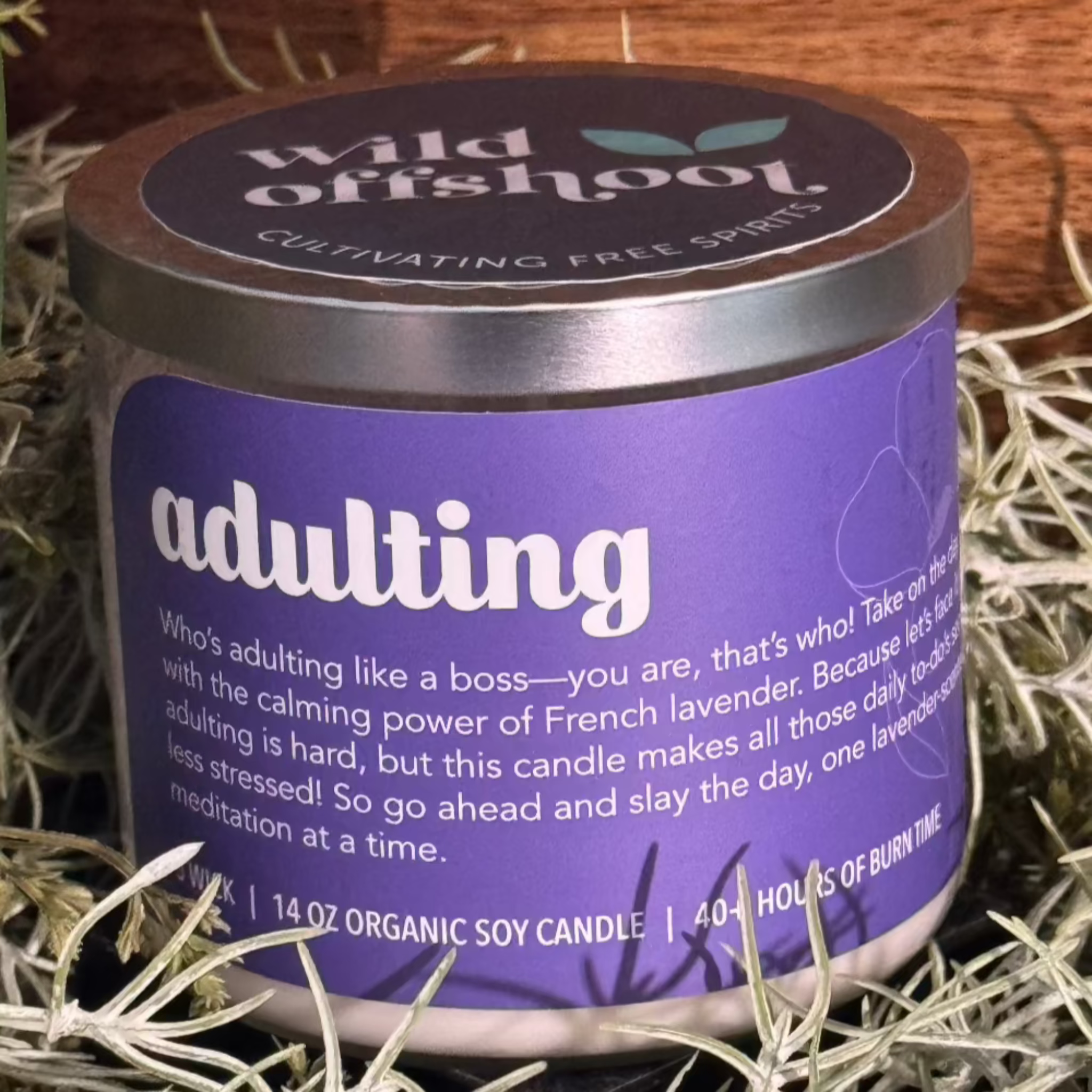 This image features a charming "Adulting" themed French lavender candle, presented in a clear glass jar with a stylish silver metal lid. The candle is made from organic soy wax and weighs 14 oz, offering up to 40 hours of burn time.