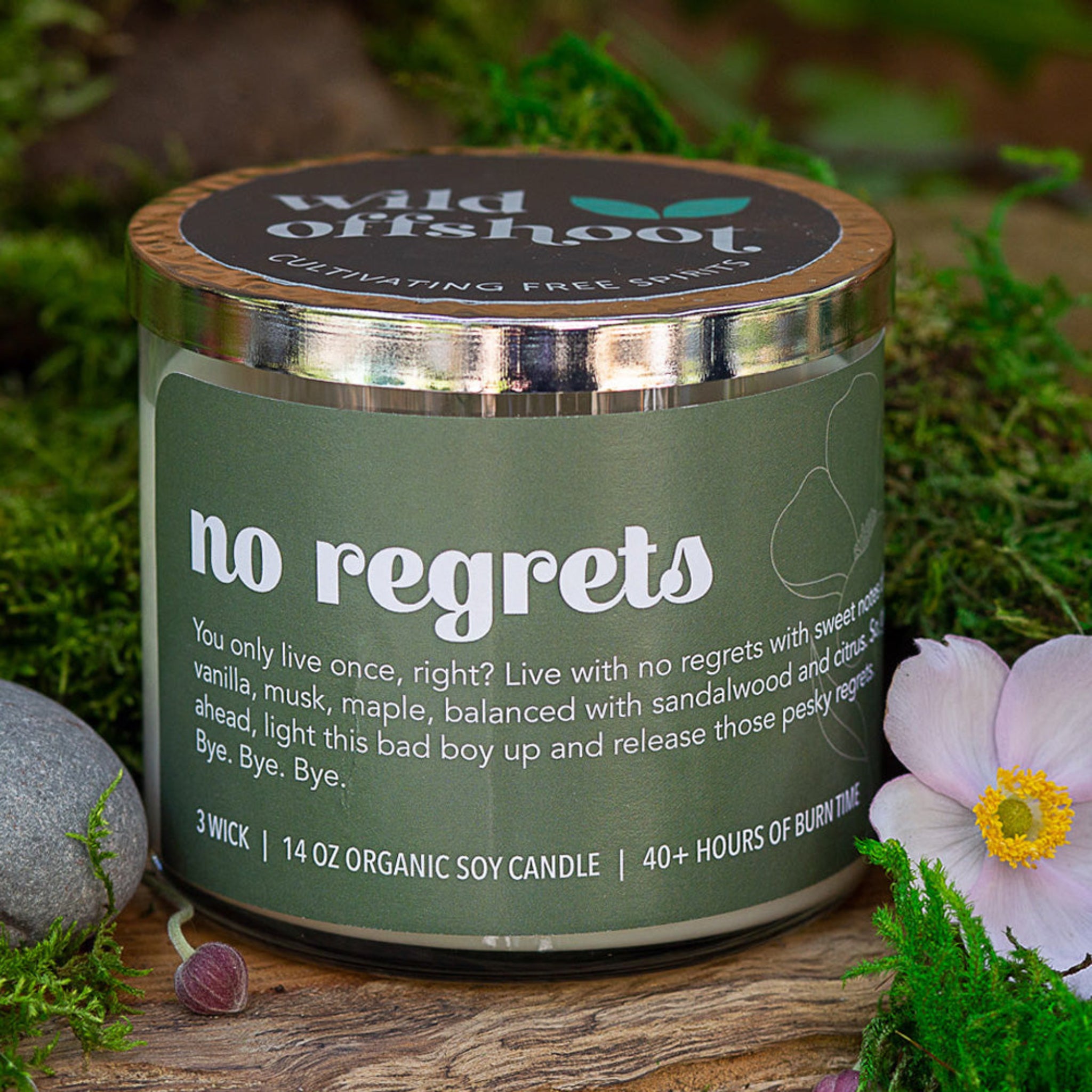 A green glass jar 14 oz candle with a silver metal lid, labeled 'No Regrets' with the brand 'Wild Offshoot' on the label. Three wicks and 40 hours of burn time.
