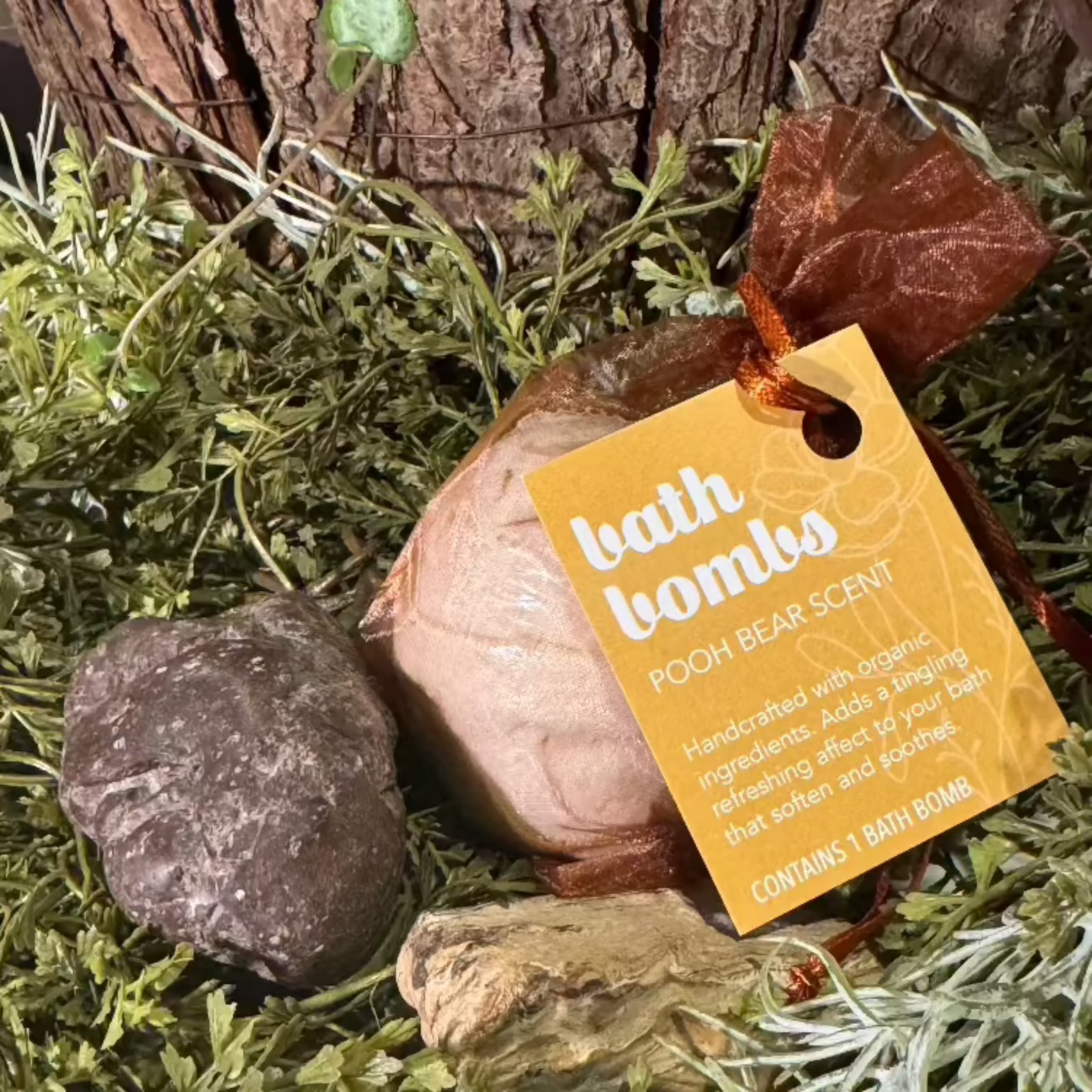 A bath bomb with a label that reads 'Pooh Bear - with oatmeal and honey aroma. The bath bomb is presented in a decorative setting with greenery.