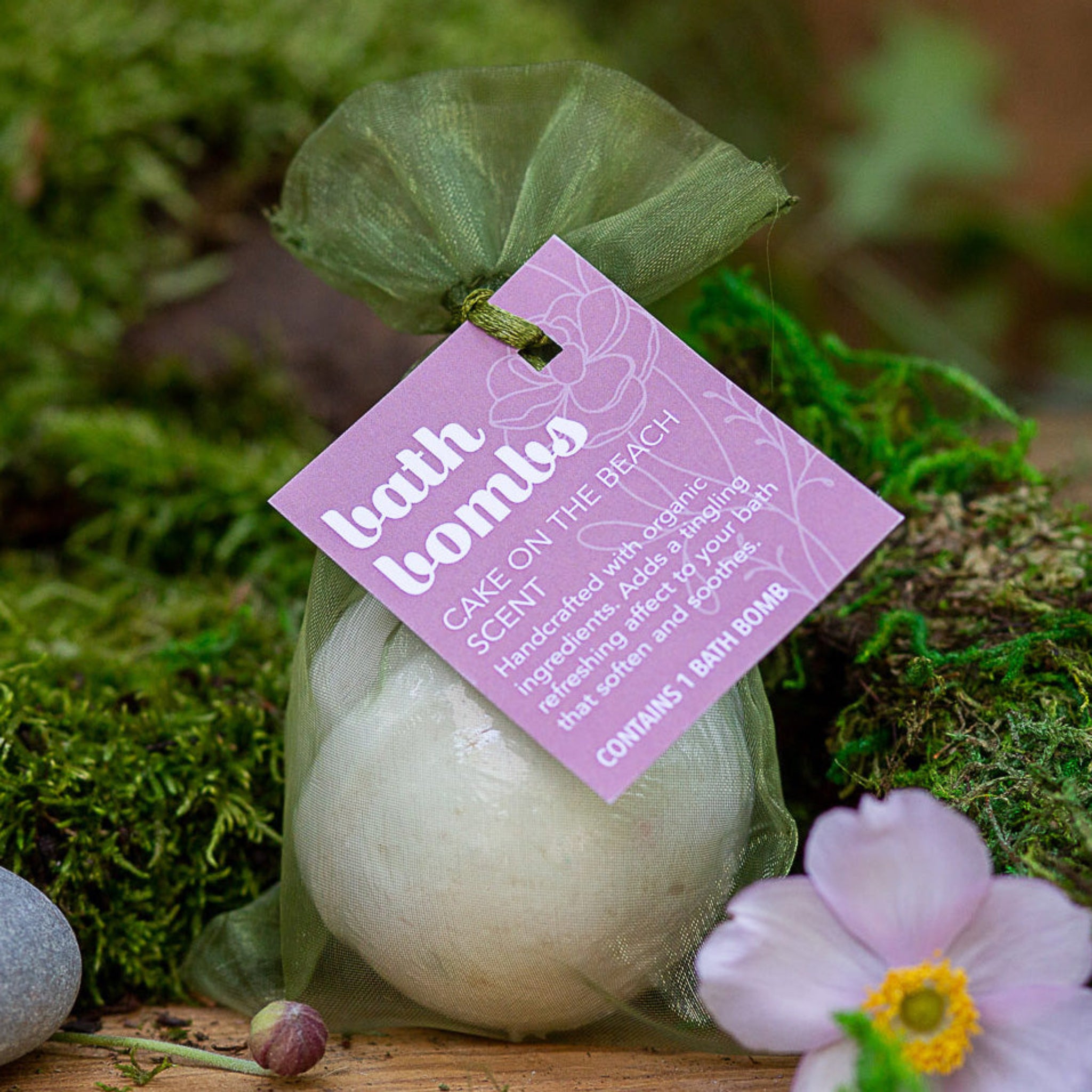 Wild Offshoot Cake on the Beach scent bath bomb - packaged in a green sheer bag with a label.