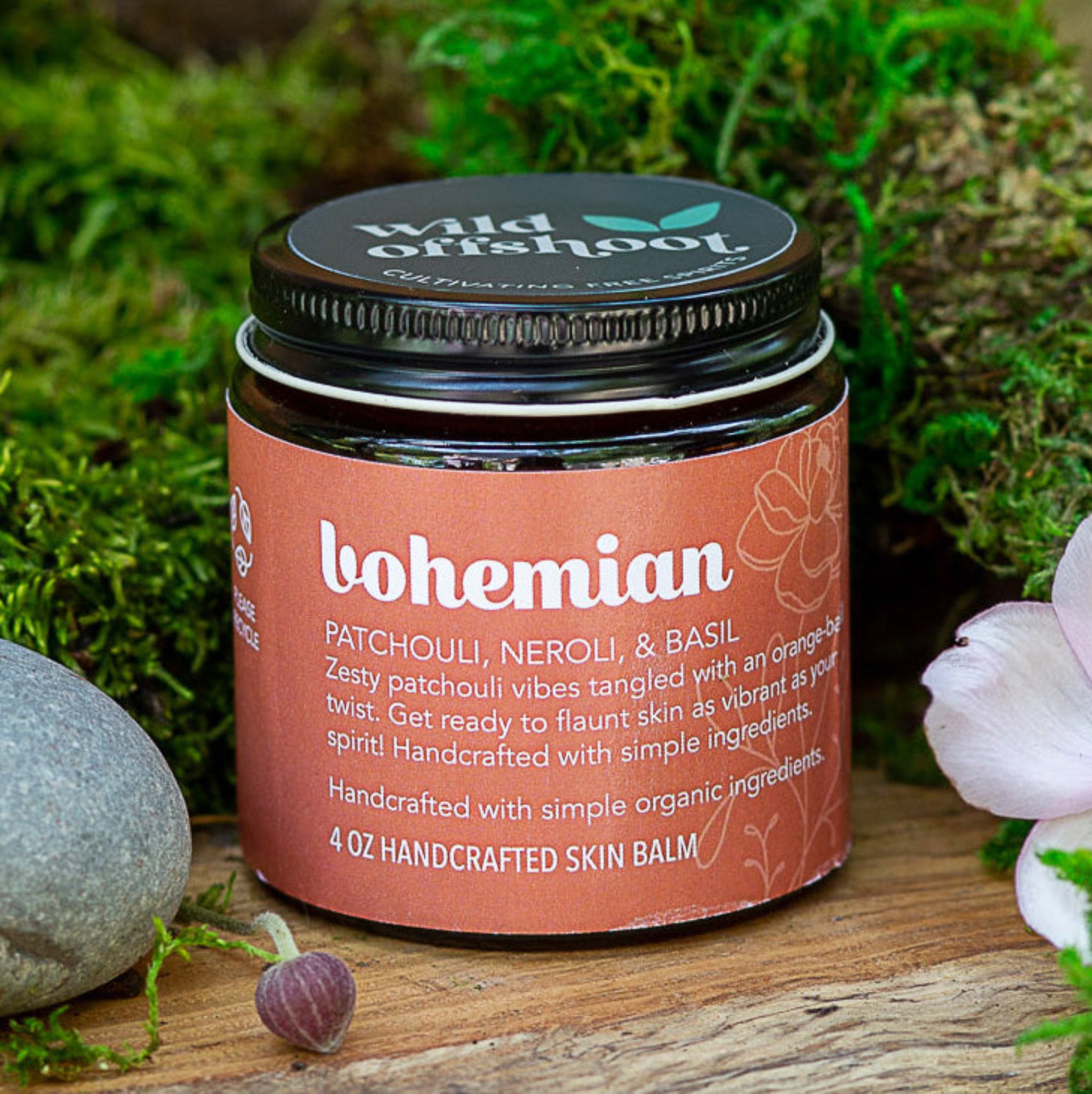 A 4oz jar of 'Bohemian Body Balm' by Wild Offshoot, surrounded by floral elements in a natural outdoor setting.
