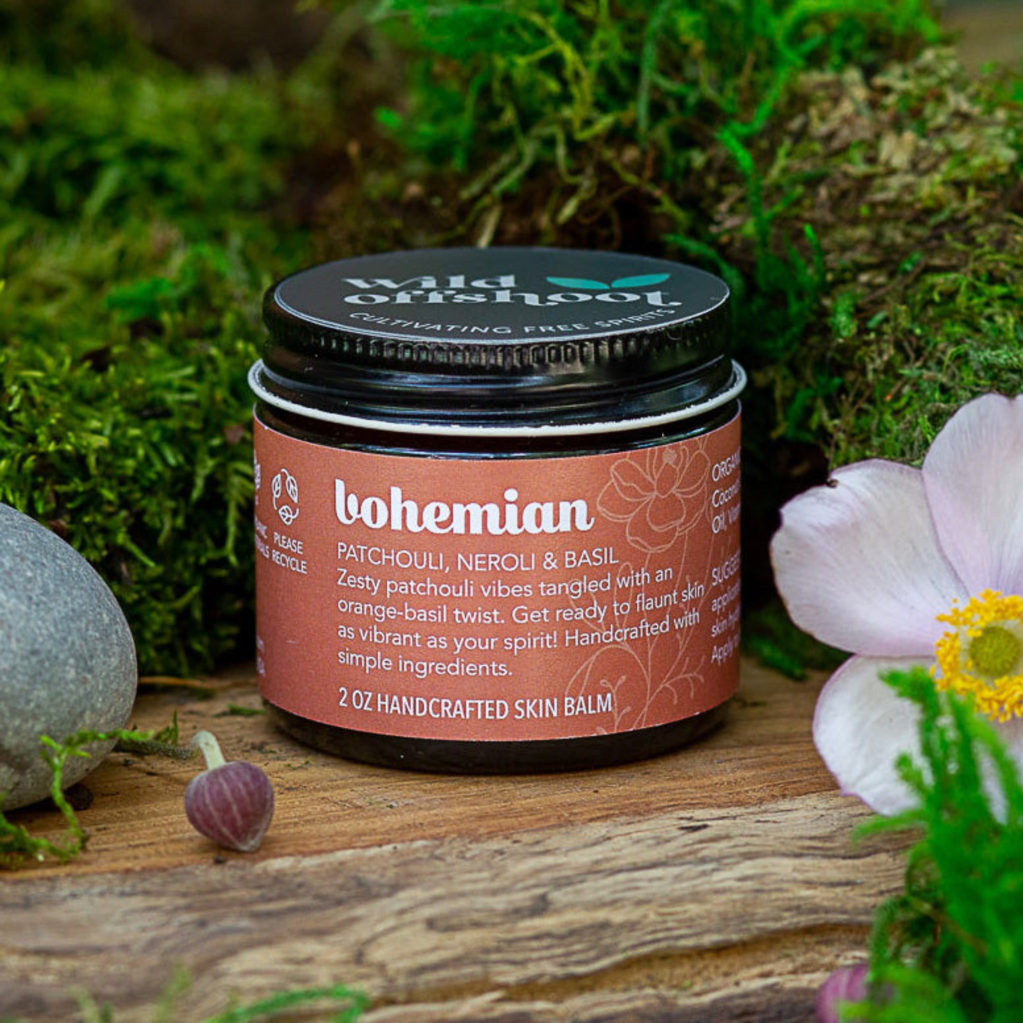 A 2 oz jar of 'Bohemian Body Balm' by Wild Offshoot, surrounded by floral elements in a natural outdoor setting.