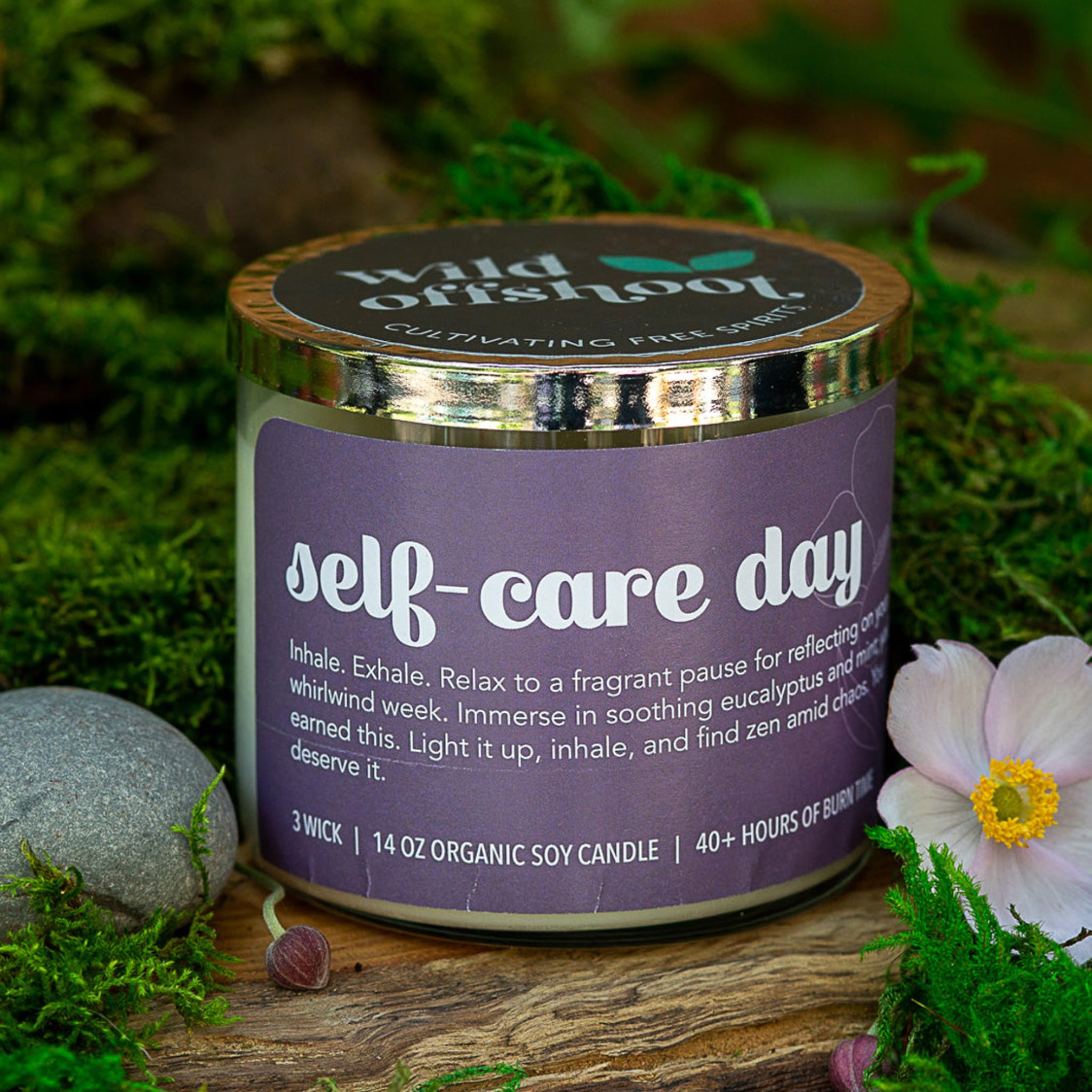 A purple soy wax 14 oz candle with a label that reads 'Self-Care Day - Inhale. Exhale three wick with 40 hours of burn time.